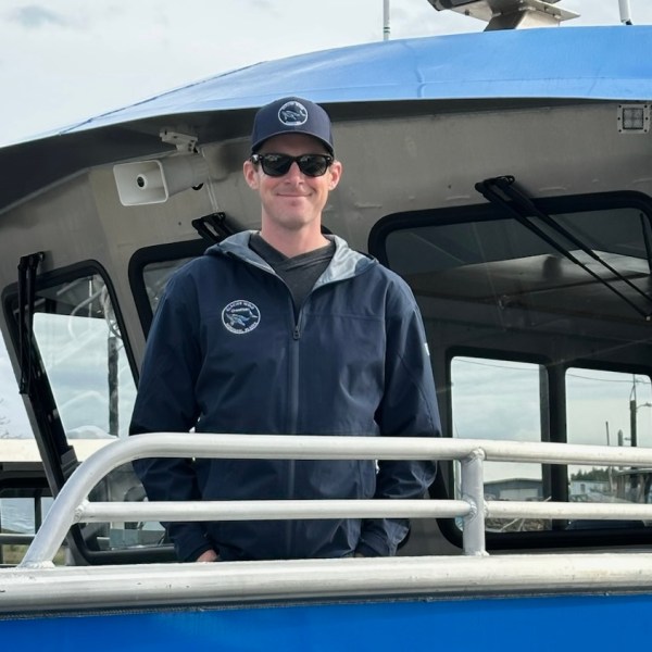IMG_7966 Person in navy jacket and cap stands on a boat with a blue canopy.